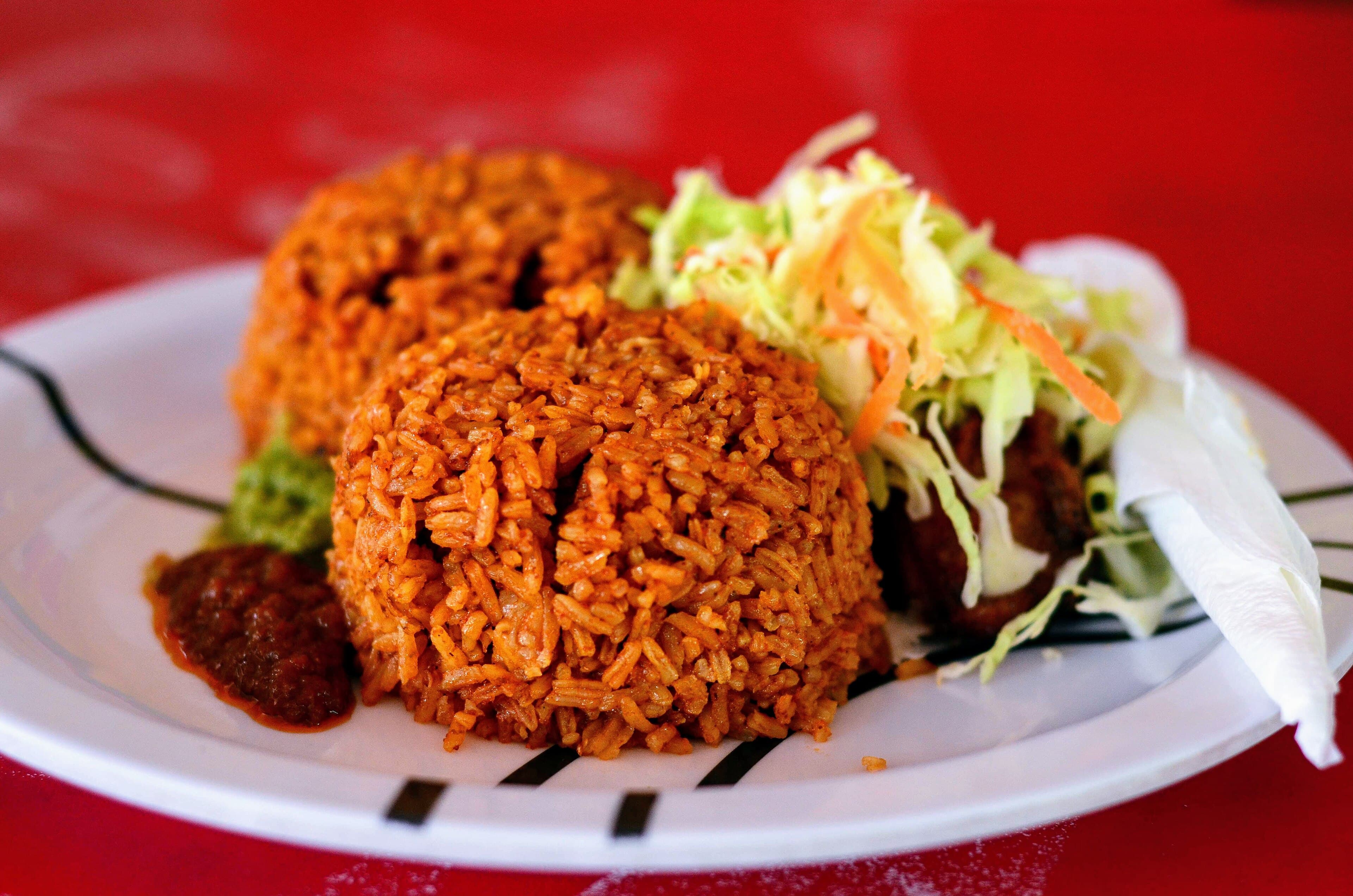A large pot of golden-orange Malian jollof rice steaming on an outdoor stove