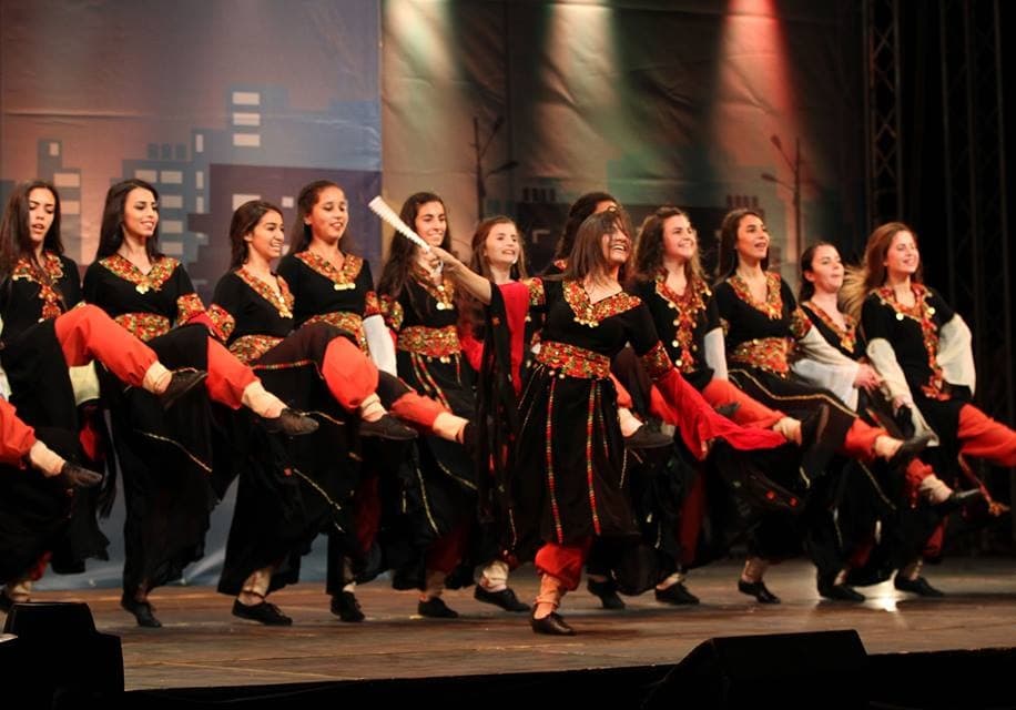 A line of young dancers in traditional dress performing dabke with arms linked