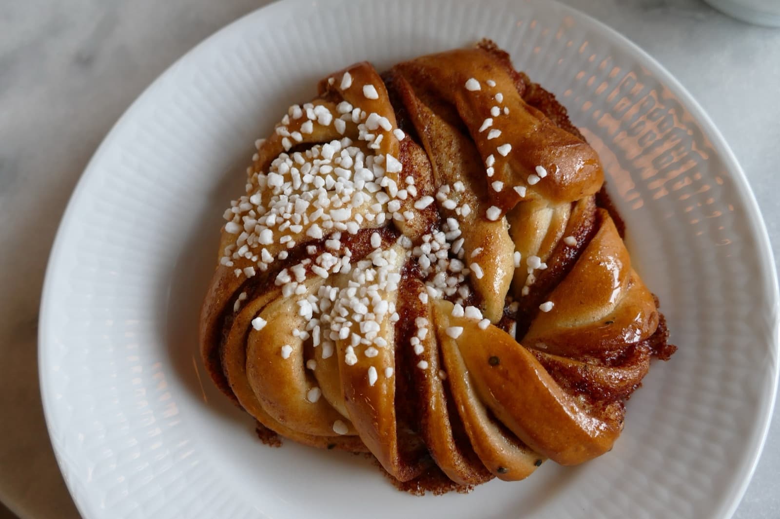 A classic Swedish cinnamon bun (kanelbulle) topped with pearl sugar