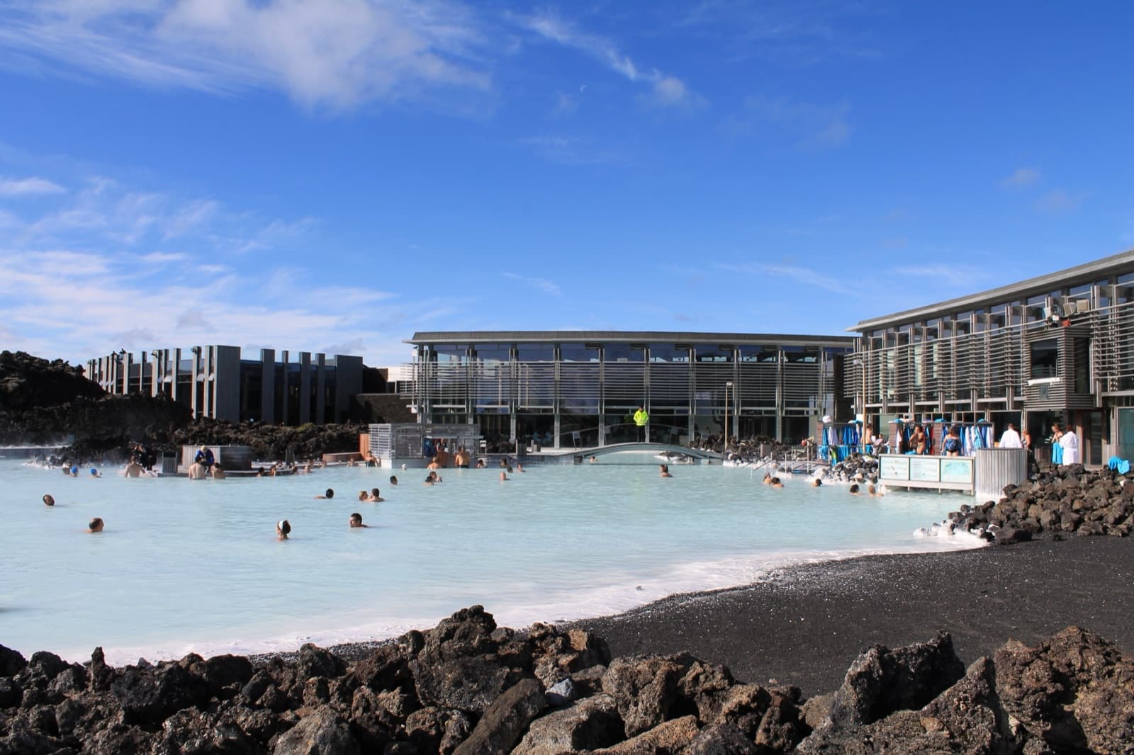 The pale milky-blue water of the Blue Lagoon with black lava rocks around the edge