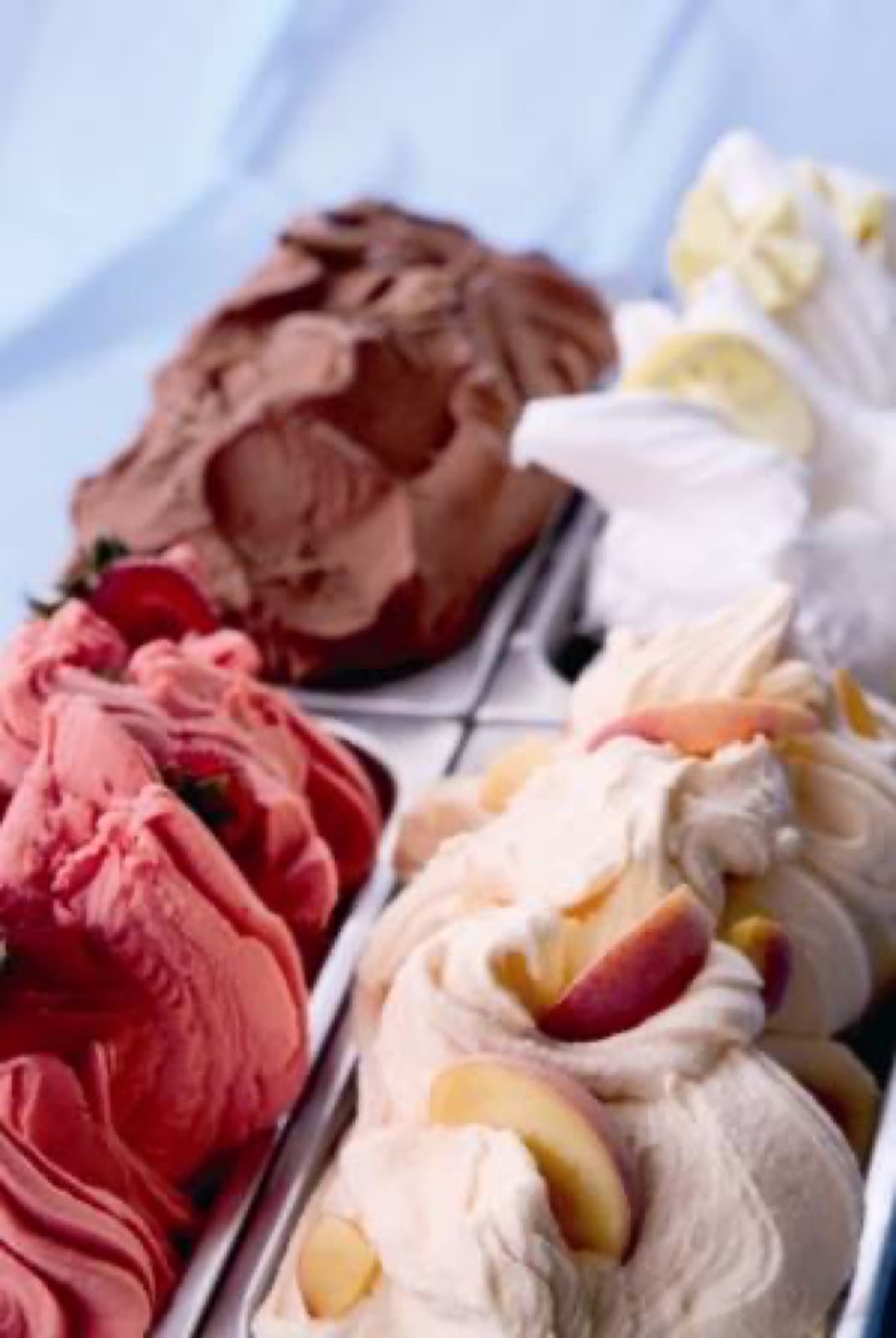 Tubs of pink strawberry, brown chocolate, white vanilla and peach gelato