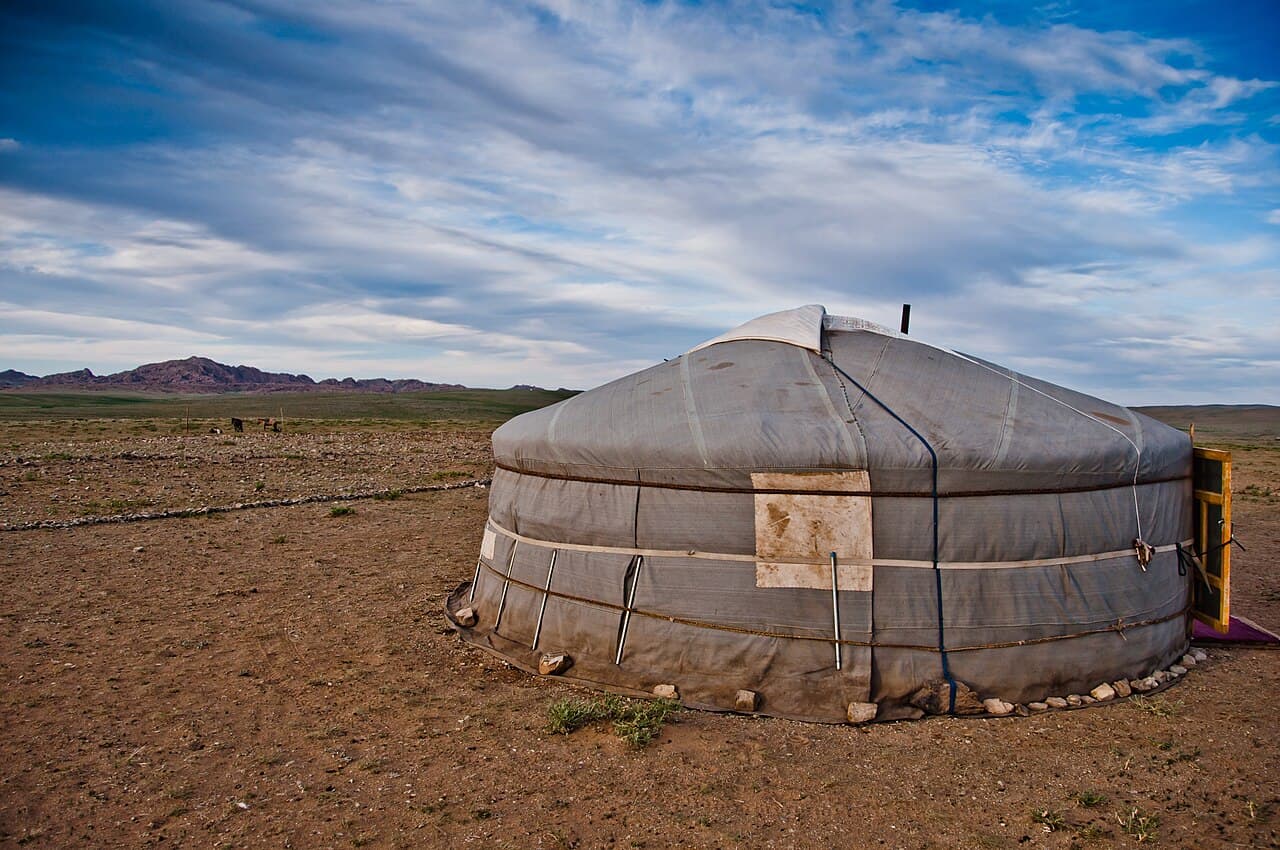 A white felt ger sitting on the Mongolian steppe with mountains behind