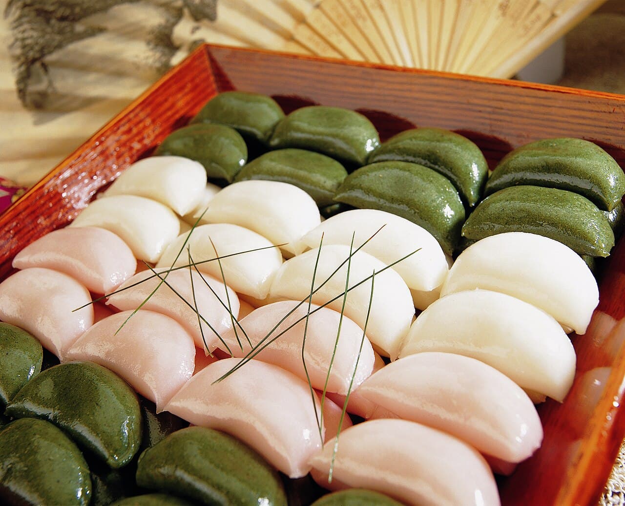 A box of brightly coloured pink, white and green half-moon rice cakes called songpyeon