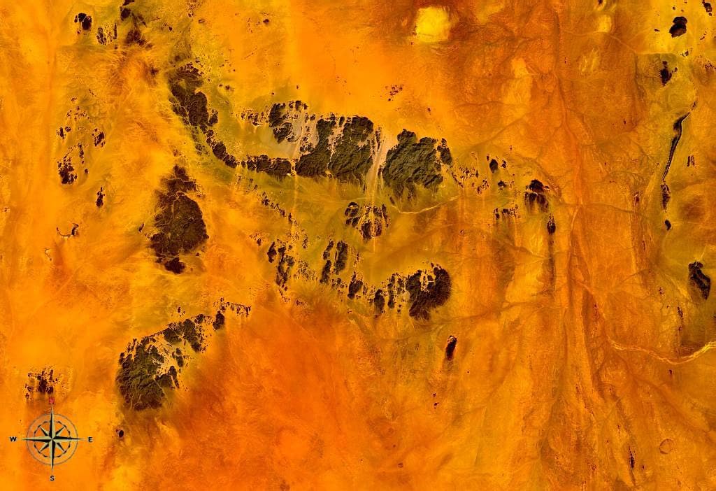 Golden sand dunes and bare rock ridges of the Nubian Desert under a bright blue sky