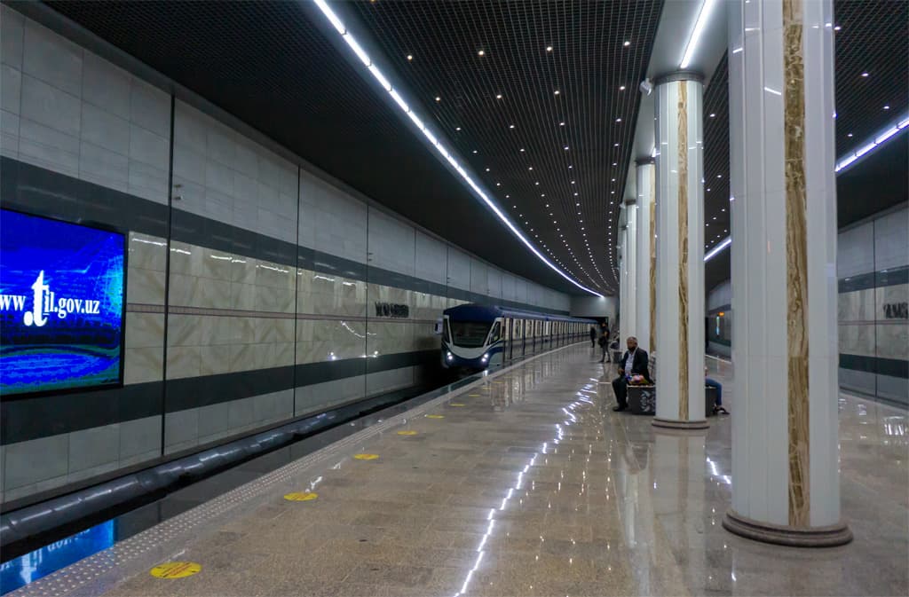 A grand, brightly lit station in the Tashkent metro with painted ceilings and decorated columns